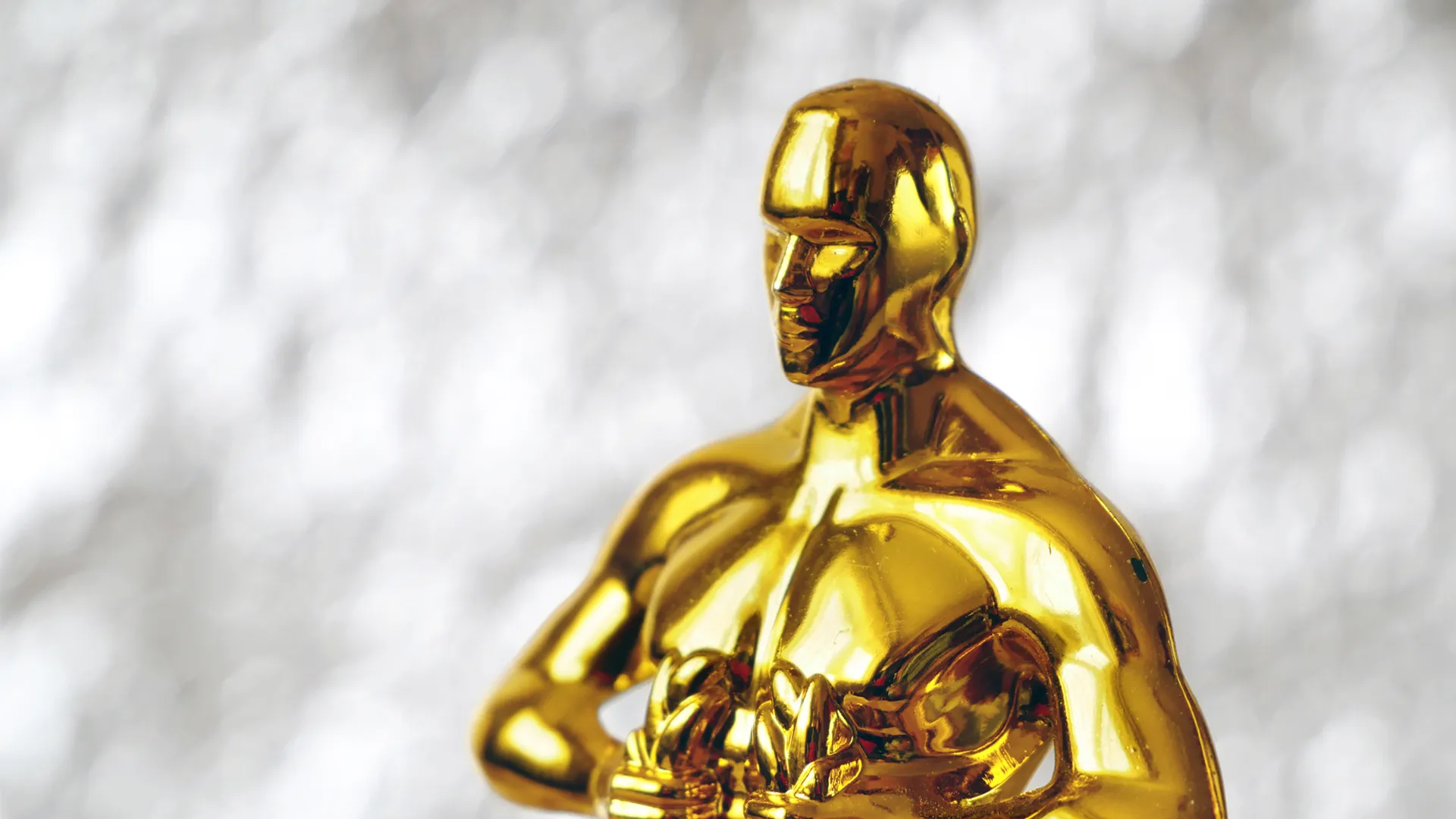 A gold Oscar statue in front of a gray background.